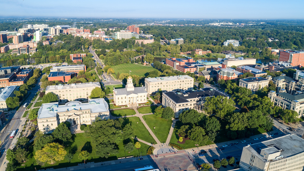 An aerial photograph of the University of Iowa campus taken in the morning, facing west toward the Iowa River and the health sciences campus beyond
